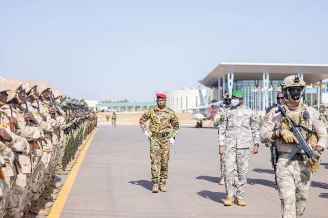 Le général Assimi Goïta, président de la transition au Mali, passe en revue des troupes en tenue militaire avec un béret vert et un cache-nez
