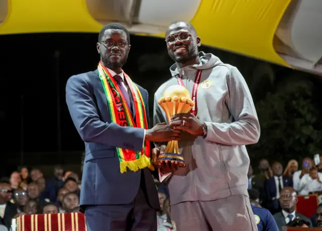 Le président du Sénégal Bassirou Diomaye Faye et le capitaine Khalidou Koulibaly tenant ensemble le trophée de la Coupe d'Afrique des Nations